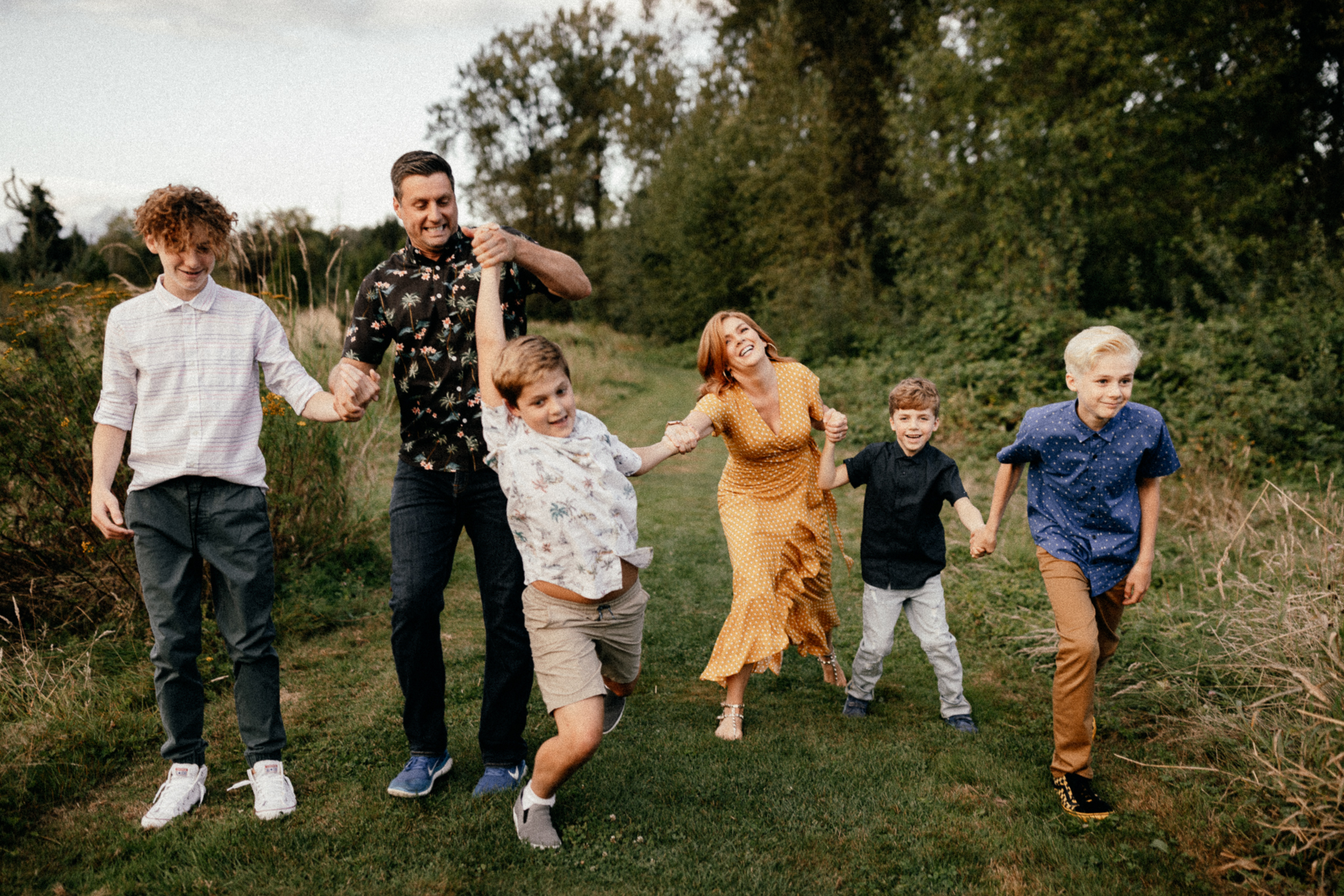 Mom, dad, and four sons walking through the grass and being silly together.